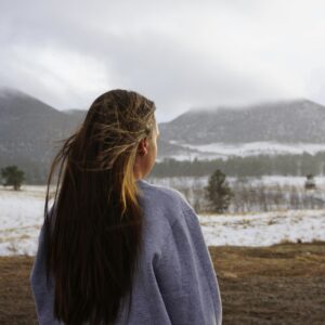 A woman in a sweatshirt gazing at a winter mountain landscape, enveloped in serene beauty.
