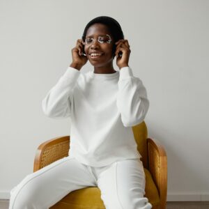 Smiling woman sitting on a chair wearing white with face paint, enjoying music indoors.